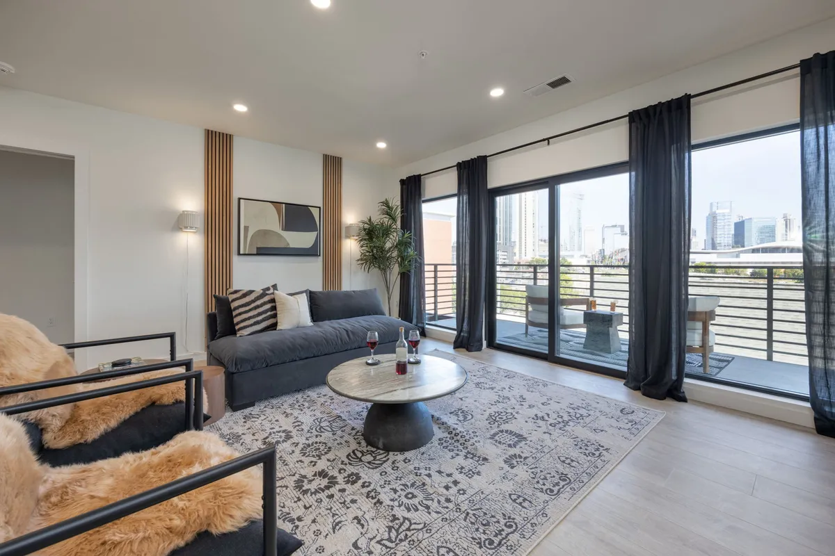 A stylish lounge area with a comfortable sofa, coffee table, large windows, and decorative art. The space feels cozy and contemporary, ideal for relaxing or socializing with friends while enjoying views of the city.