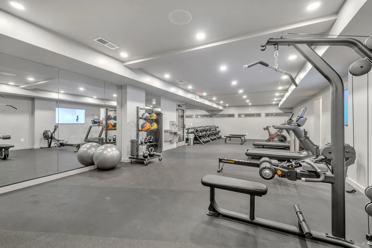 A modern gym interior filled with various exercise equipment including mirrors, exercise balls, and weight racks. The setting is bright and energetic, with ample space for both solo workouts and group fitness activities.