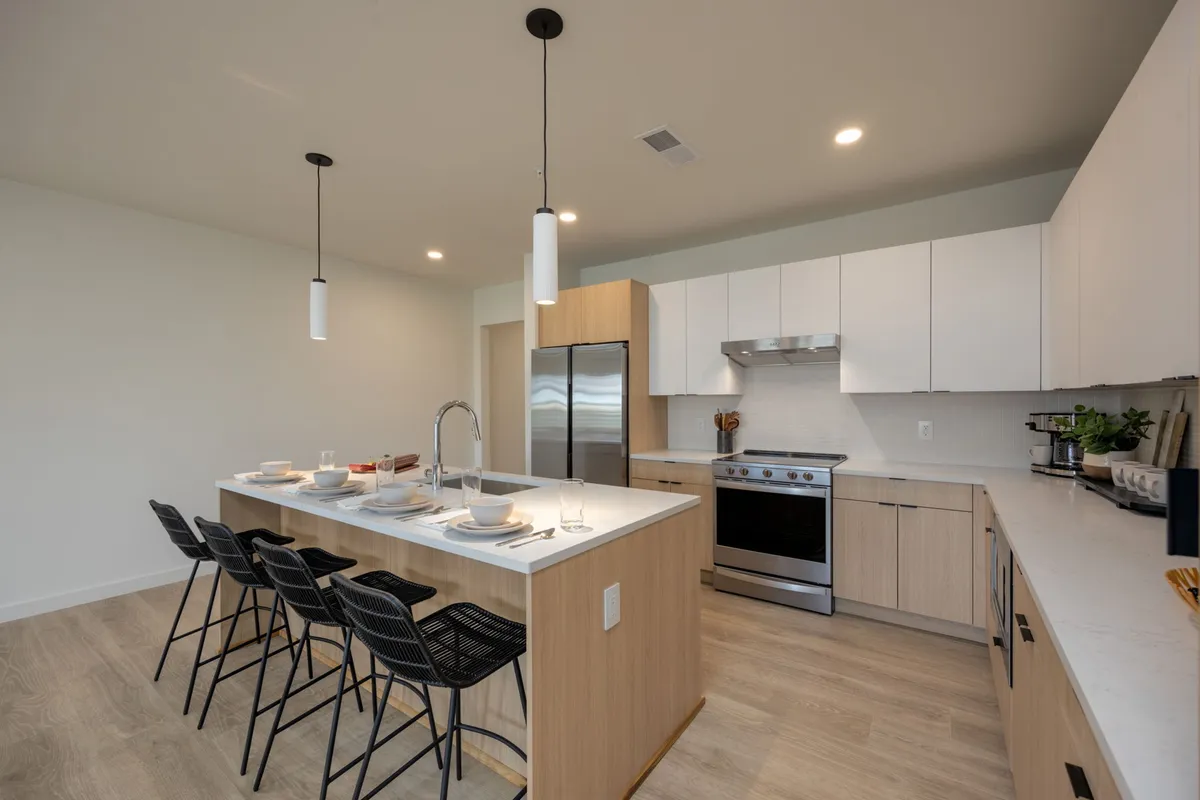 A sleek, modern kitchen with an island countertop, modern appliances, and bar stools, surrounded by cabinetry and decorative touches. The space is both functional for cooking and inviting for entertaining.
