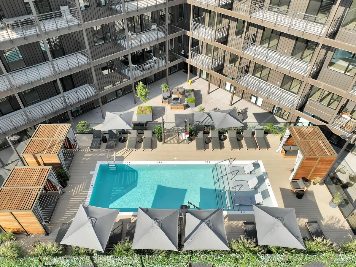 A beautifully landscaped pool area features modern cabana structures, plush lounge chairs, and lush greenery. The space is designed for sunbathing, swimming, and casual gatherings, with sunset light enhancing the inviting atmosphere. The overall mood is one of comfort, leisure, and community.