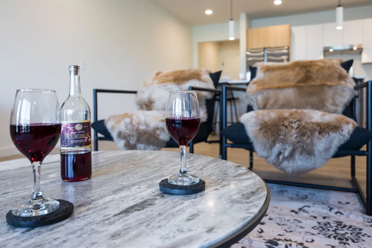 A cozy, sophisticated living area featuring modern chairs, a coffee table topped with wine glasses and a bottle, and luxurious faux fur throws. The lighting and styling evoke a sense of privacy and comfort, reflecting a high standard of hospitality.