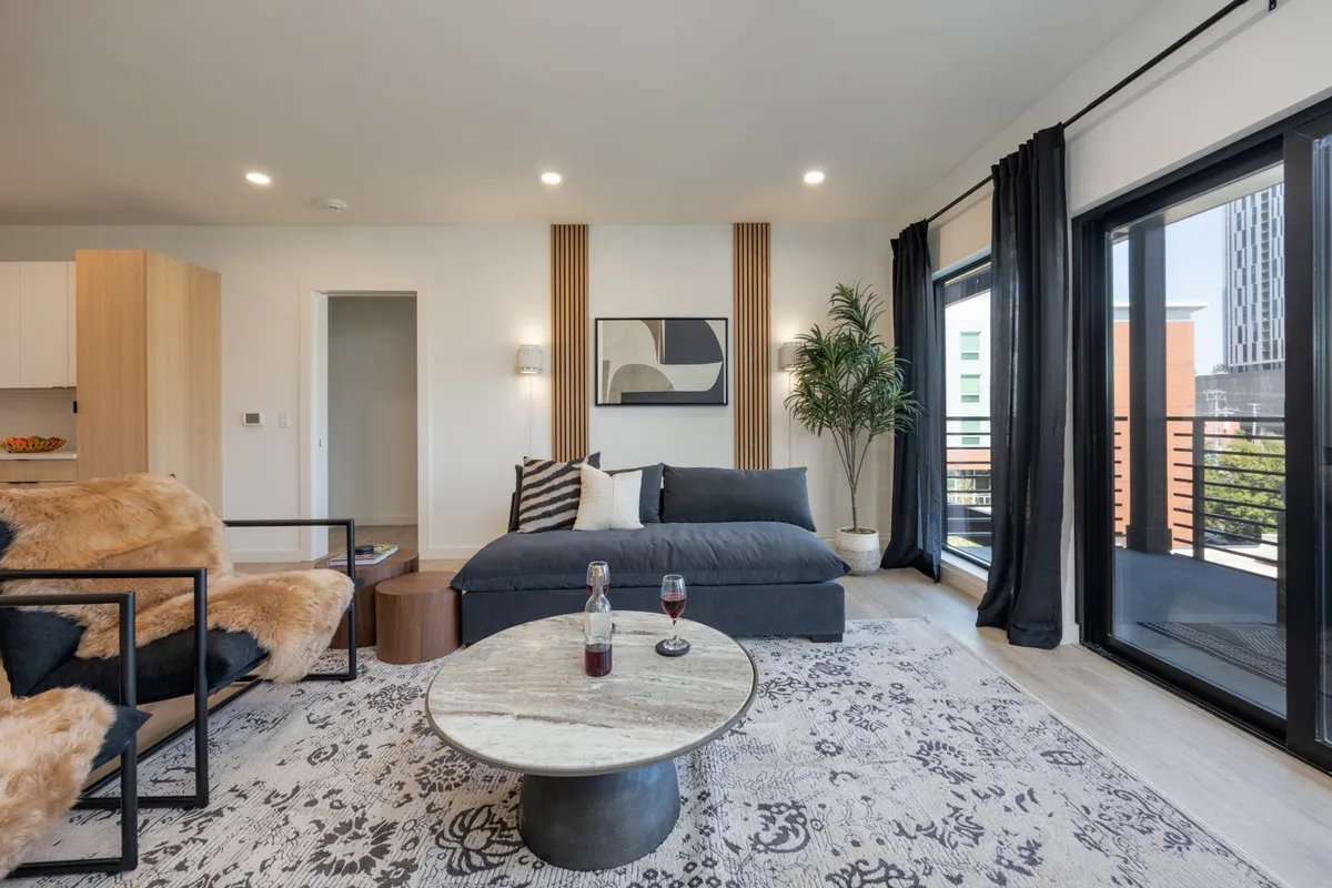 A modern, inviting living room with a plush sofa, contemporary artwork, a sleek coffee table, and a potted plant. The setup suggests both relaxation and a welcoming space for guests, consistent with professional management and guest comfort.